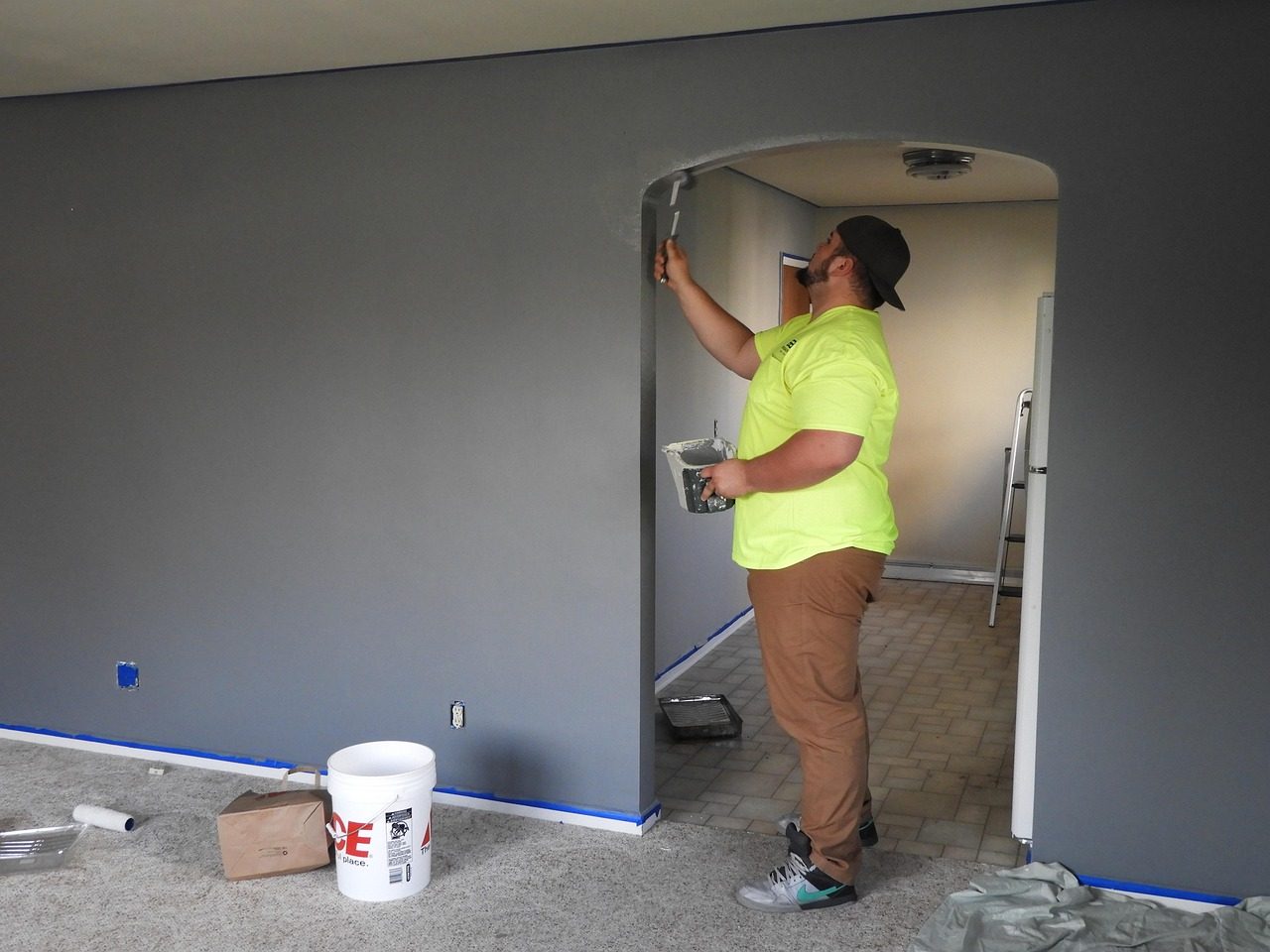 Audubon Woods Neighborhood property maintenance features a Handyman painting the walls and archway between two rooms in a bluish gray color.