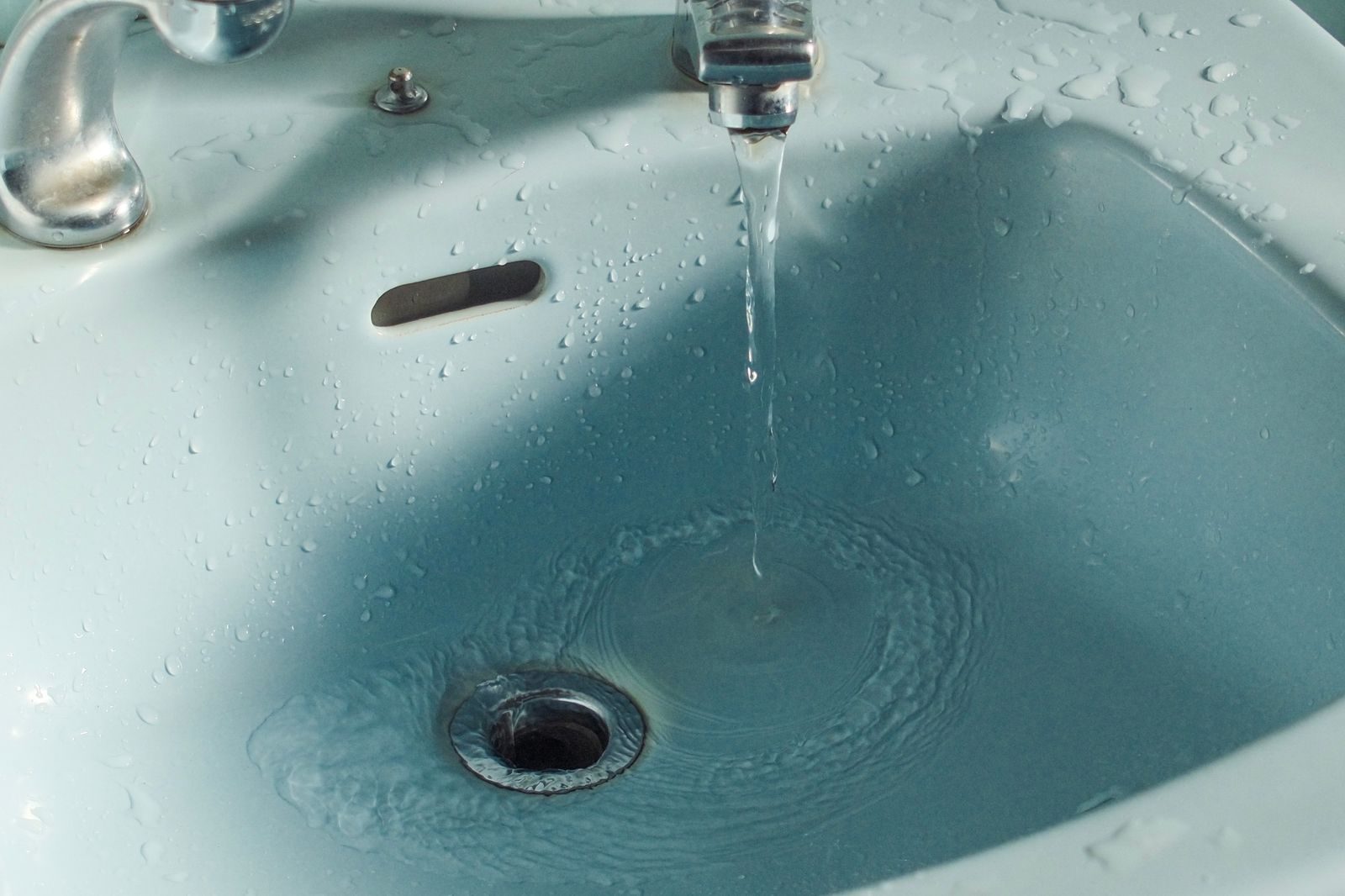 Unclogging a slow bathroom sink drain Close-up of water flowing from a faucet into a bathroom sink.