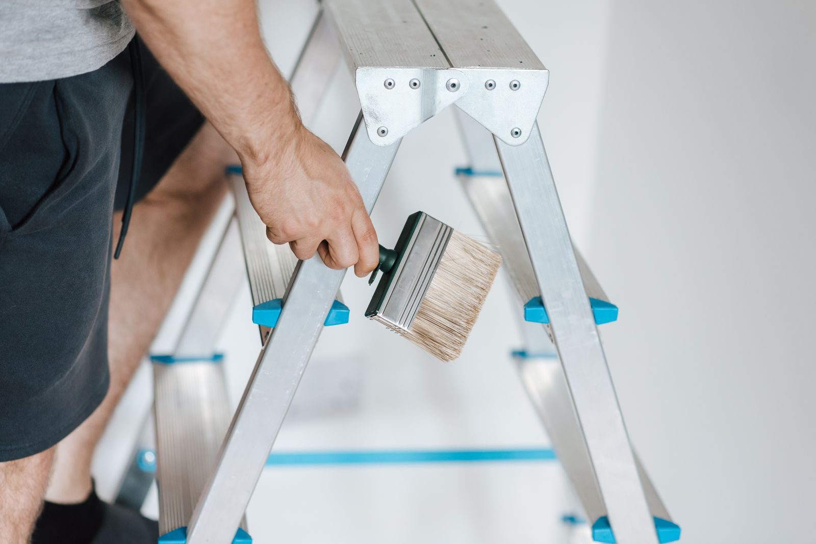 Side view of crop anonymous male master standing on ladder with tool while painting walls in flat near Baron Estates Neighborhood handyman services