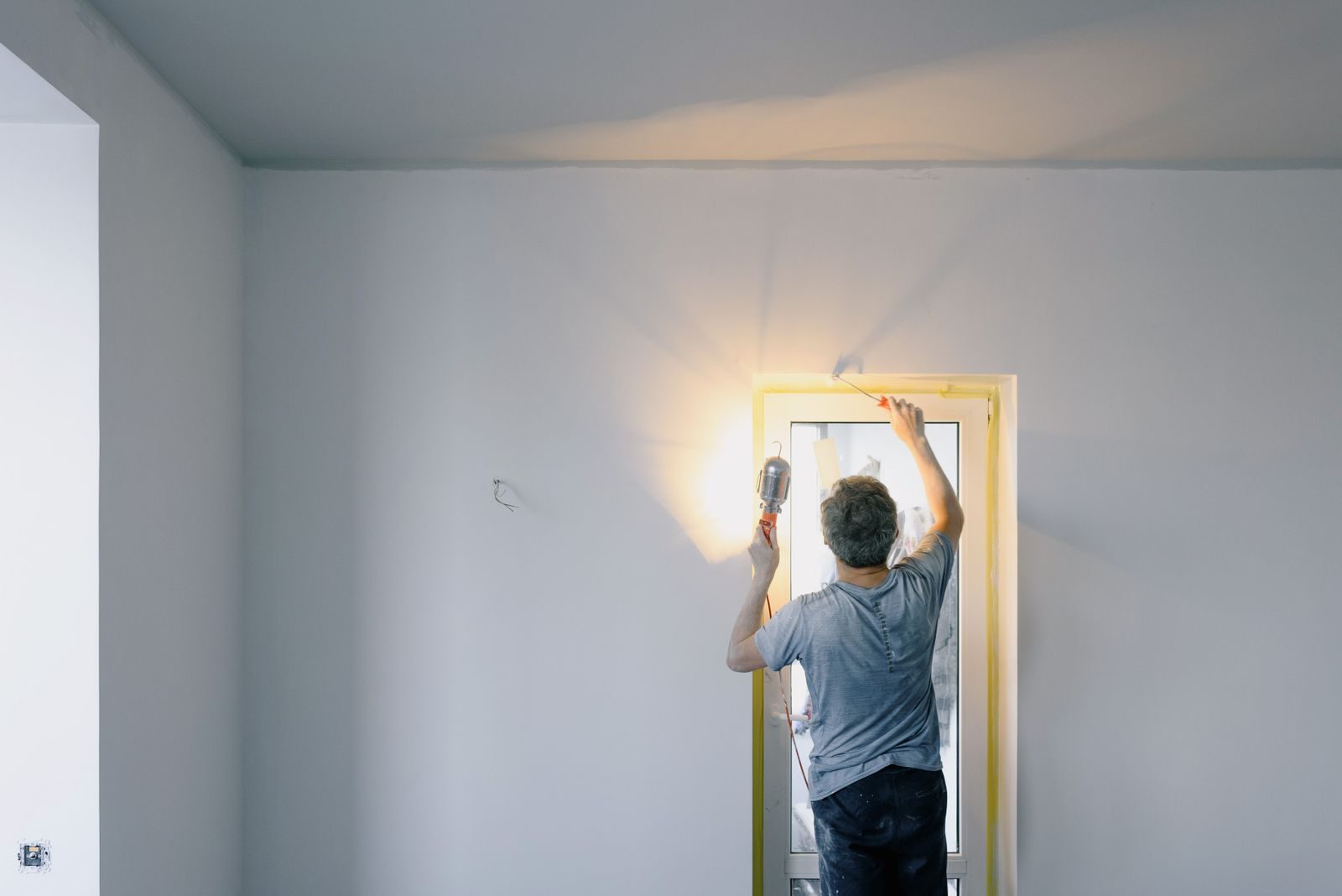 City Center Neighborhood repair specialist back view of unrecognizable male in dirty clothes holding bright lamp while repairing door at home