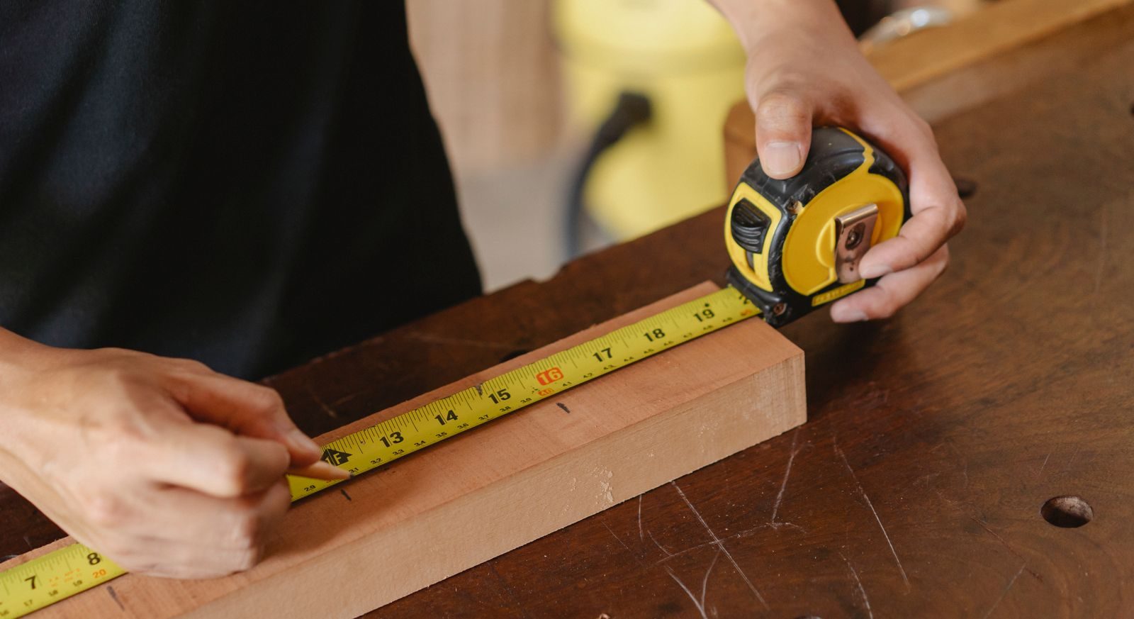 Bishop Gate Neighborhood handyman services Accurate unrecognizable male worker with pencil and measuring tape on wooden board standing near workbench during work process on blurred background