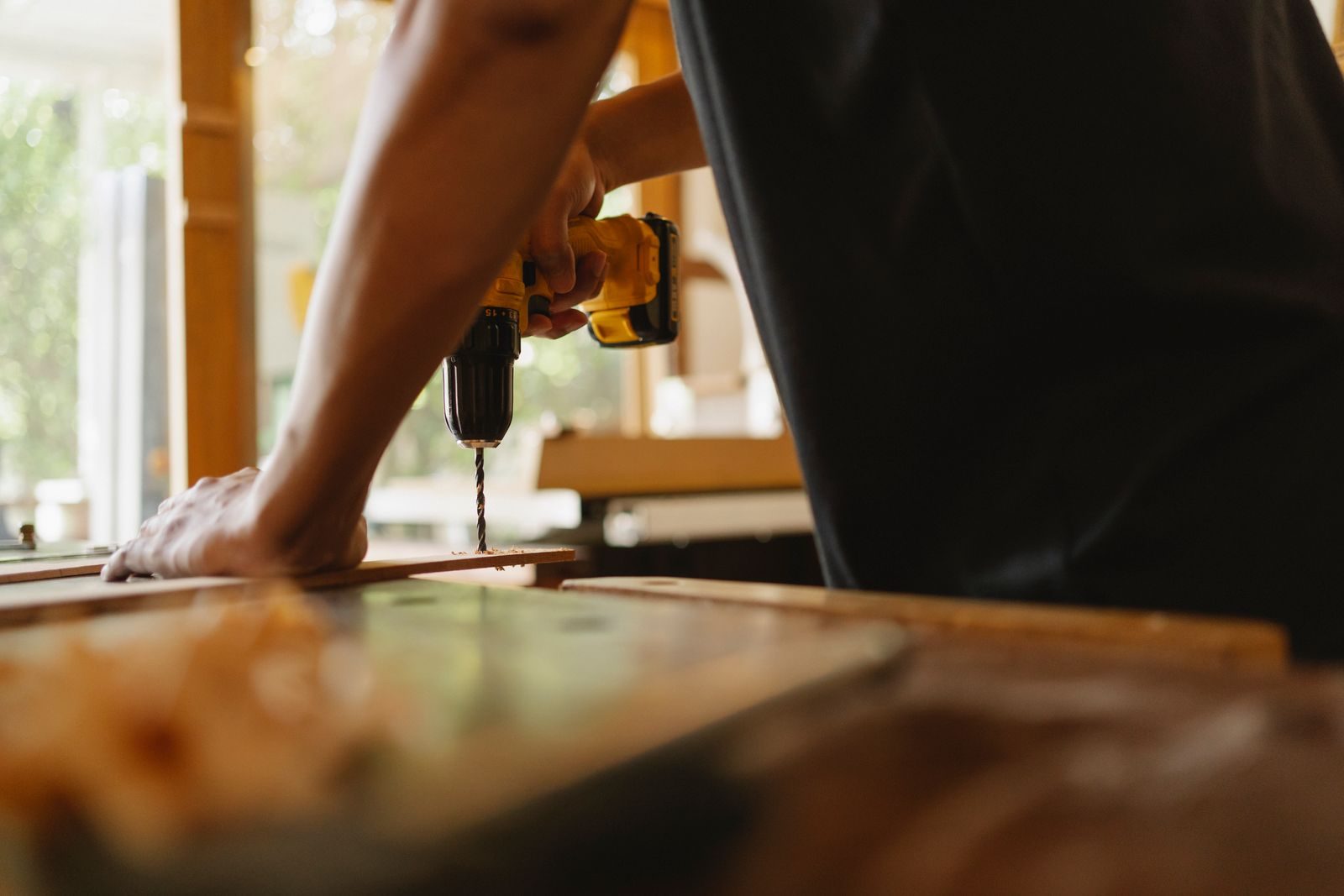 Bartlett Highlands Neighborhood building services anonymous male carpenter making hole on wooden plank with drill during work in studio on sunny day
