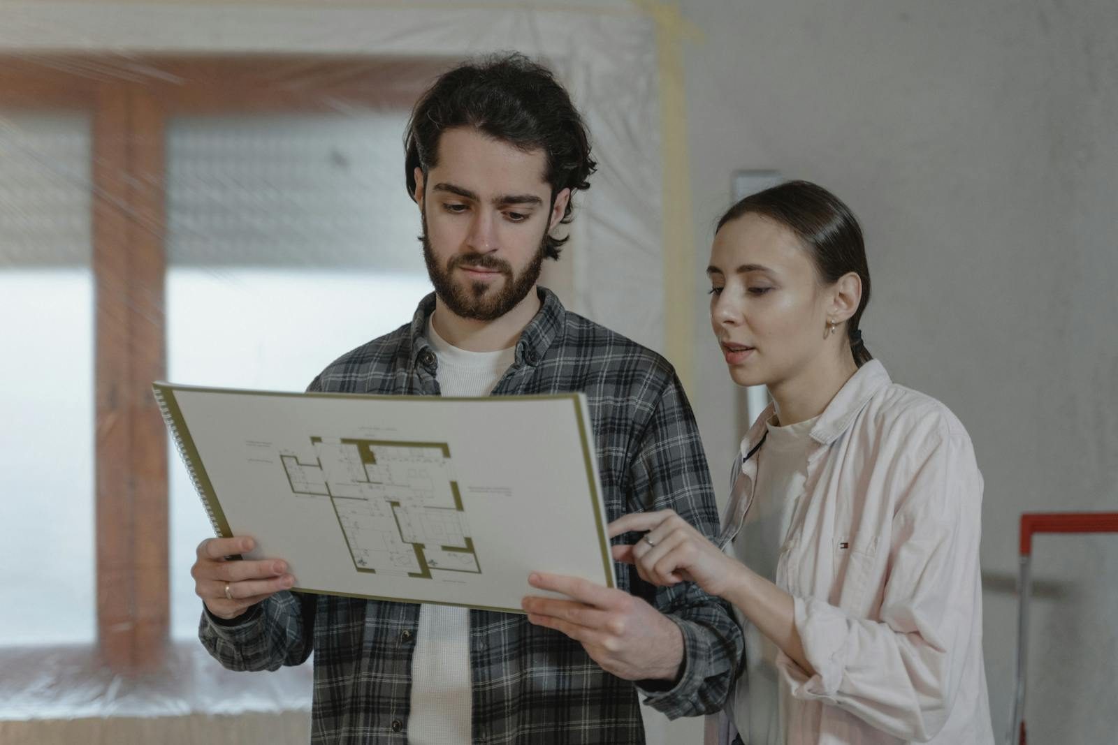 Bayliss Neighborhood contractor services man and woman examining a floor plan for home improvement indoors.