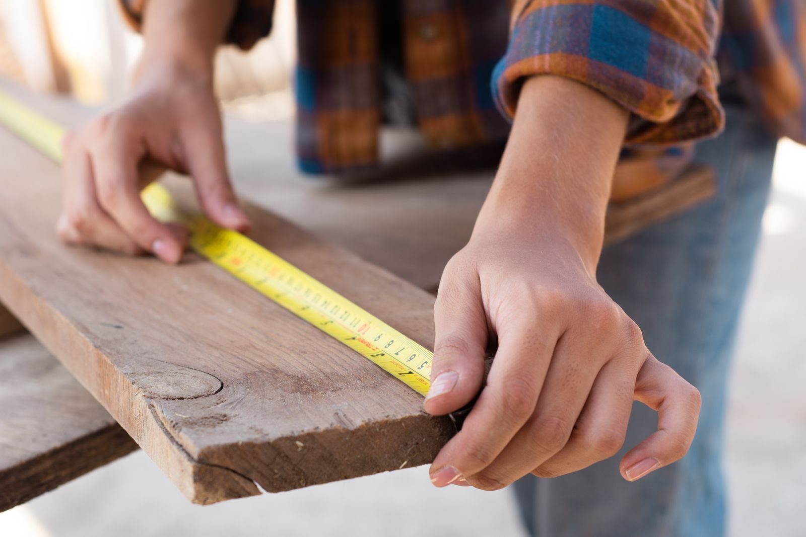 Buntyn Neighborhood carpentry services Close-up of hands measuring a wooden plank with a tape measure in a carpentry setting.