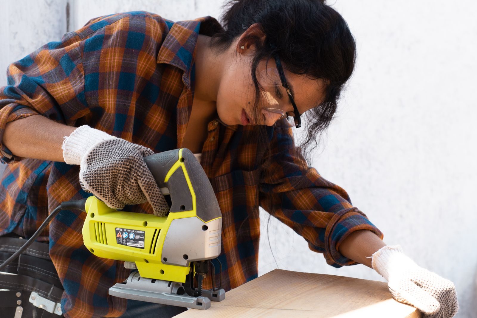 Bartlett Road Corridor Neighborhood renovation services focused woman uses an electric jigsaw on a wood piece, embodying DIY craftsmanship.