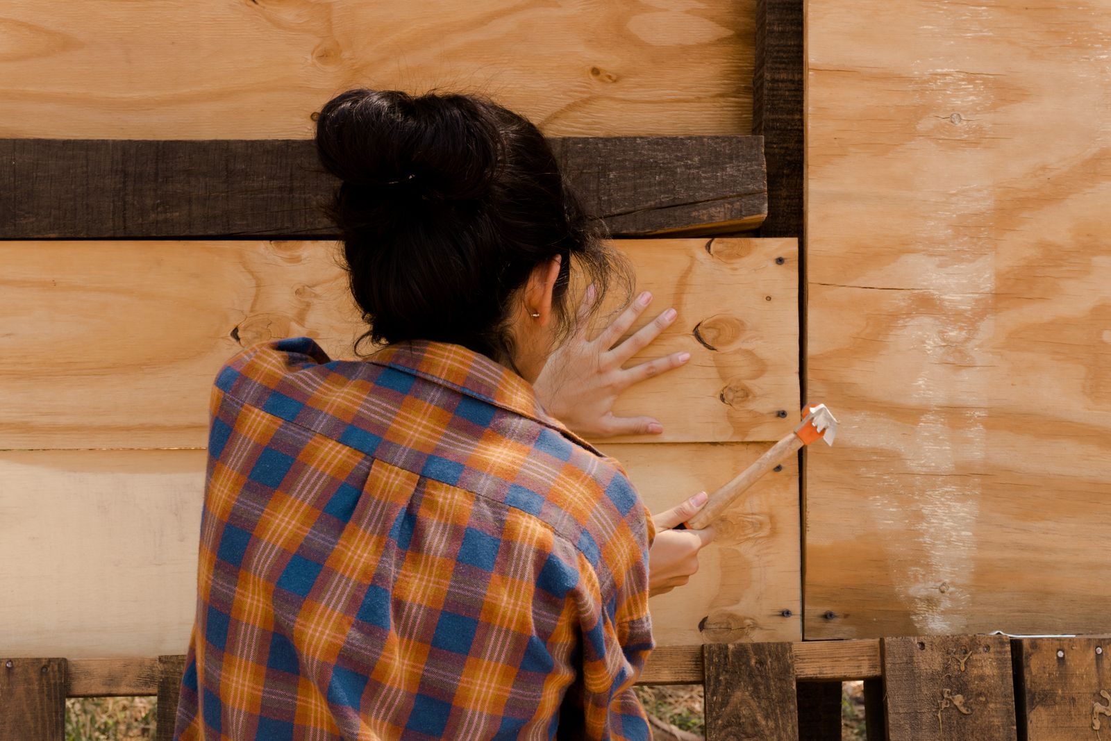 Brookmeade Neighborhood home improvement A woman in a plaid shirt expertly hammering a wooden plank. Empowerment in carpentry.