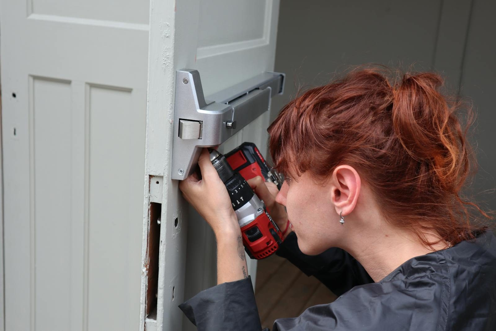 Bartlett Corporate Park Neighborhood repair contractor caucasian woman focusing on door installation with power drill, side view.